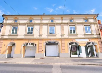 Historisches Gebäude mit einer hellen Fassade, großen Fenstern und drei Garagentoren im Erdgeschoss.