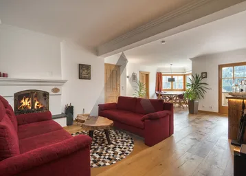 Gemütlicher Wohn-Essbereich mit Kamin, Holzboden und roten Sofas, ideal für entspannte Abende.