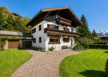 Traditionelles alpenländisches Haus mit weißer Fassade, Holzbalkonen und gepflegtem Vorgarten.
