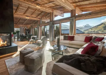 Großzügiger Wohn- und Essbereich mit Kamin, Holzbalkendecke und Panoramablick auf die Berge.