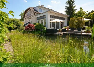 Großzügiger Gartenbereich mit Teich und Holzdeck, umgeben von üppiger Vegetation und dem Haus.