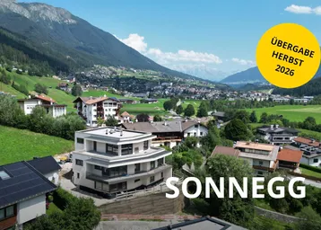 Luftaufnahme eines modernen Neubaus in einer malerischen Berglandschaft mit umliegenden Häusern und grünen Hügeln.