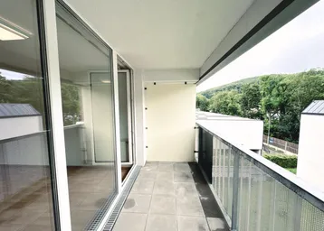 Geräumiger Balkon mit Fliesenboden und Blick ins Grüne sowie auf umliegende Gebäude.