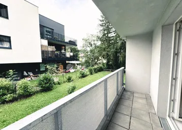 Balkon mit Fliesenboden und Blick auf den Gemeinschaftsgarten und angrenzende Gebäude.