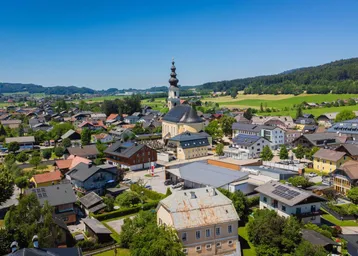 Panoramablick auf eine malerische Stadt mit Kirche, umgeben von grünen Feldern und sanften Hügeln.