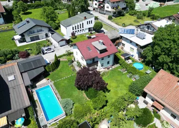 Luftaufnahme einer Wohnsiedlung mit grünen Gärten, Bäumen und einem Swimmingpool.