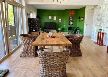 Geräumiger Wohn- und Essbereich mit Holztisch, Korbstühlen und grüner Akzentwand.