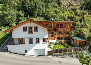 Charmantes Haus im alpinen Stil mit weißer Fassade, Holzverkleidung und integrierter Garage.