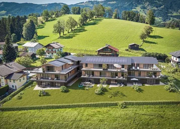 Moderne Wohngebäude mit Holzfassaden und Solaranlagen, eingebettet in eine grüne Hügellandschaft.