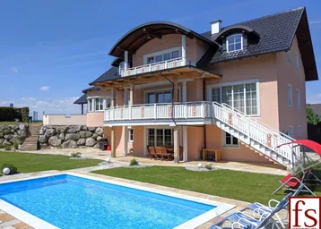 Großzügiges Einfamilienhaus mit weitläufigem Garten, privatem Pool und mehreren Balkonen unter blauem Himmel.
