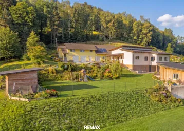 Drohnenaufnahme eines Anwesens mit mehreren Gebäuden, großem Garten und Spielplatz, umgeben von Wald.