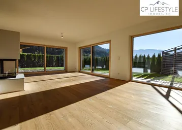 Helles Wohnzimmer mit Holzboden, modernem Kamin und großen Schiebetüren zur Terrasse mit Bergblick.