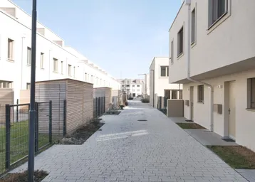 Reihenhausanlage mit gepflastertem Weg und kleinen Vorgärten in einer modernen Siedlung.