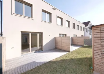 Moderne Reihenhausfassade mit Holzterrasse, Rasenfläche und Sichtschutz im Außenbereich.