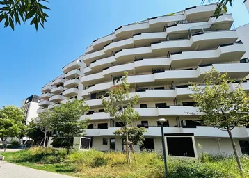 Moderne Wohnanlage mit geschwungenen Balkonen und begrünten Außenbereichen unter blauem Himmel.