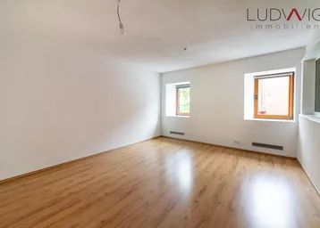 Helles, leeres Zimmer mit Laminatboden und weißen Wänden, bereit zur individuellen Gestaltung.