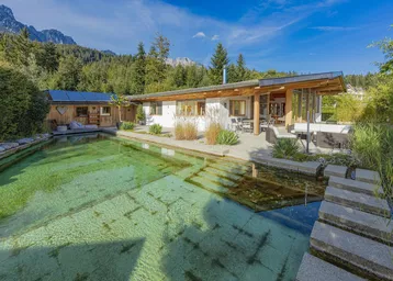 Modernes Haus mit Naturpool, großer Terrasse, Bergblick und Photovoltaikanlage in grüner Umgebung.