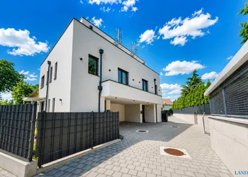 Modernes Mehrfamilienhaus mit weißer Fassade, Carport und gepflasterter Zufahrt unter blauem Himmel.