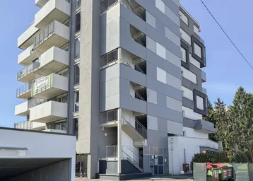 Modernes Mehrfamilienhaus mit mehreren Balkonen und einer Tiefgaragenzufahrt.