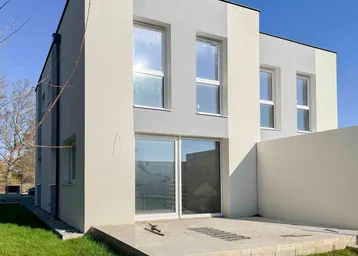 Moderne Neubaufassade mit großen Fenstern und einer kleinen Terrasse im Erdgeschoss.