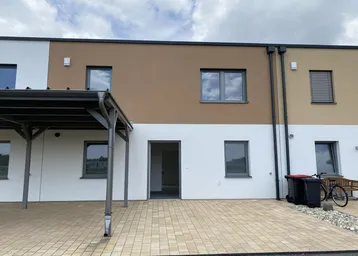 Mehrere Reihenhäuser mit Carport und gepflasterter Terrasse im Außenbereich.