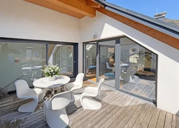 Sonnige Dachterrasse mit Holzboden, modernen Gartenmöbeln und Zugang zum Innenbereich.