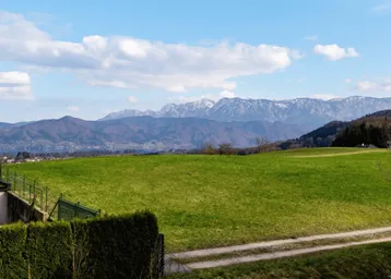 Weitläufiger Blick über grüne Hügel, einen See und majestätische Berge am Horizont.