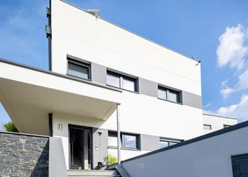 Moderne Architektur mit weißer Fassade, grauen Akzenten und einem einladenden Eingangsbereich.