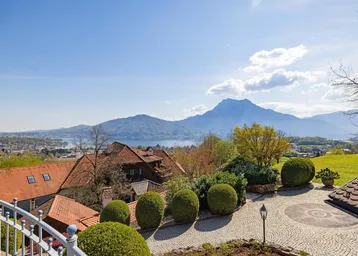 Panoramablick vom Balkon auf den See und die umliegende Berglandschaft unter blauem Himmel.