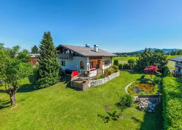 Großzügiger Gartenbereich mit Teich, Rasenfläche und einer sonnigen Terrasse mit Bergblick.