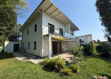 Modernes Haus mit gepflegtem Garten, Terrasse und Balkon unter strahlend blauem Himmel.
