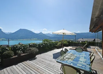 Große Holzterrasse mit Esstisch, Sonnenschirm und Liegestühlen, bietet einen atemberaubenden Blick auf den See und die Berge.