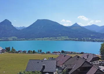 Weitläufiger Panoramablick auf einen großen See und die umliegende Berglandschaft unter blauem Himmel.