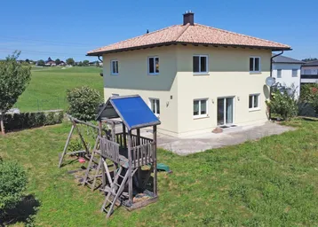 Einfamilienhaus mit großem Garten und Kinderspielplatz unter blauem Himmel.