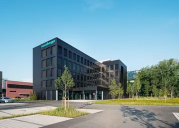 Ansicht des modernen Bürogebäudes mit dunkler Fassade und gepflegter Außenanlage unter klarem Himmel.