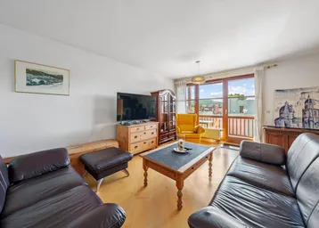 Helles Wohnzimmer mit bequemen Ledersofas, Holzboden und Zugang zum Balkon mit Weitblick.