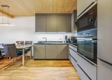 Moderne Küche mit grauen Schränken, integrierten Geräten und Essbereich.