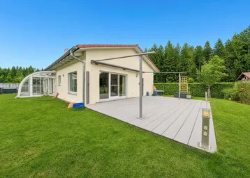 Modernes Einfamilienhaus mit großer Holzterrasse, Garten und angrenzendem Wintergarten.