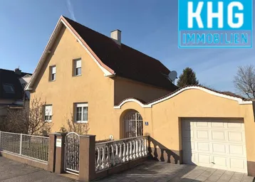 Gelbes Einfamilienhaus mit Satteldach, Garage und gepflegtem Vorgarten.