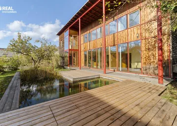 Modernes Holzhaus mit großen Glasfronten, umgeben von einem Teich und einer Holzterrasse.