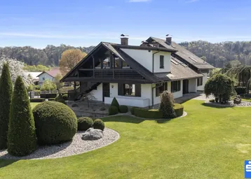 Großzügiges Anwesen mit weitläufigem Rasen und gepflegter Gartenanlage unter blauem Himmel.