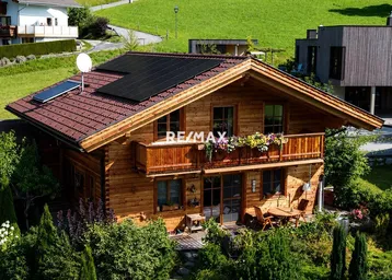 Charmantes Holzchalet mit Photovoltaikanlage, Balkon und gemütlichem Sitzbereich im Freien.