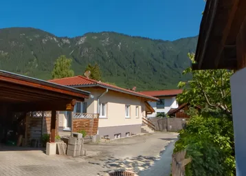 Blick auf das Haus mit Carport und der beeindruckenden Bergkulisse im Hintergrund unter blauem Himmel.