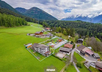 Luftaufnahme eines Anwesens in einer malerischen alpinen Landschaft mit grünen Wiesen und schneebedeckten Bergen.
