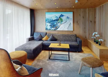 Gemütliches Wohnzimmer im alpinen Stil mit Holzwänden, bequemer Couch und Bergbild.