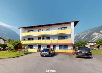 Mehrfamilienhaus mit gelben Balkonen und Bergblick in ländlicher Umgebung.