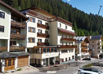 Hotelgebäude in den Bergen mit traditioneller Architektur und Balkonen, umgeben von grünen Wäldern.