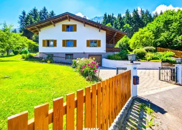 Charmantes Haus mit gepflegtem Garten, Auffahrt und Holzzaun in sonniger Berglage.