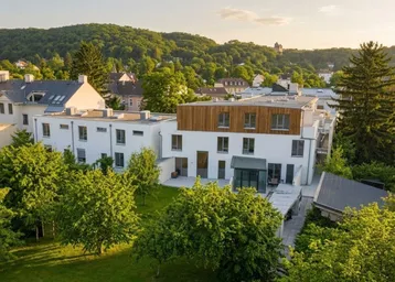 Moderne Wohnanlage mit weißer Fassade, Holzdetails und grüner Umgebung bei Sonnenuntergang.