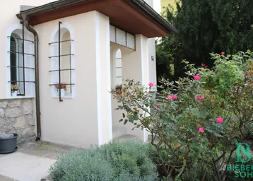 Eingangsbereich des Hauses mit dekorativen Fenstergittern und blühenden Rosenbüschen.